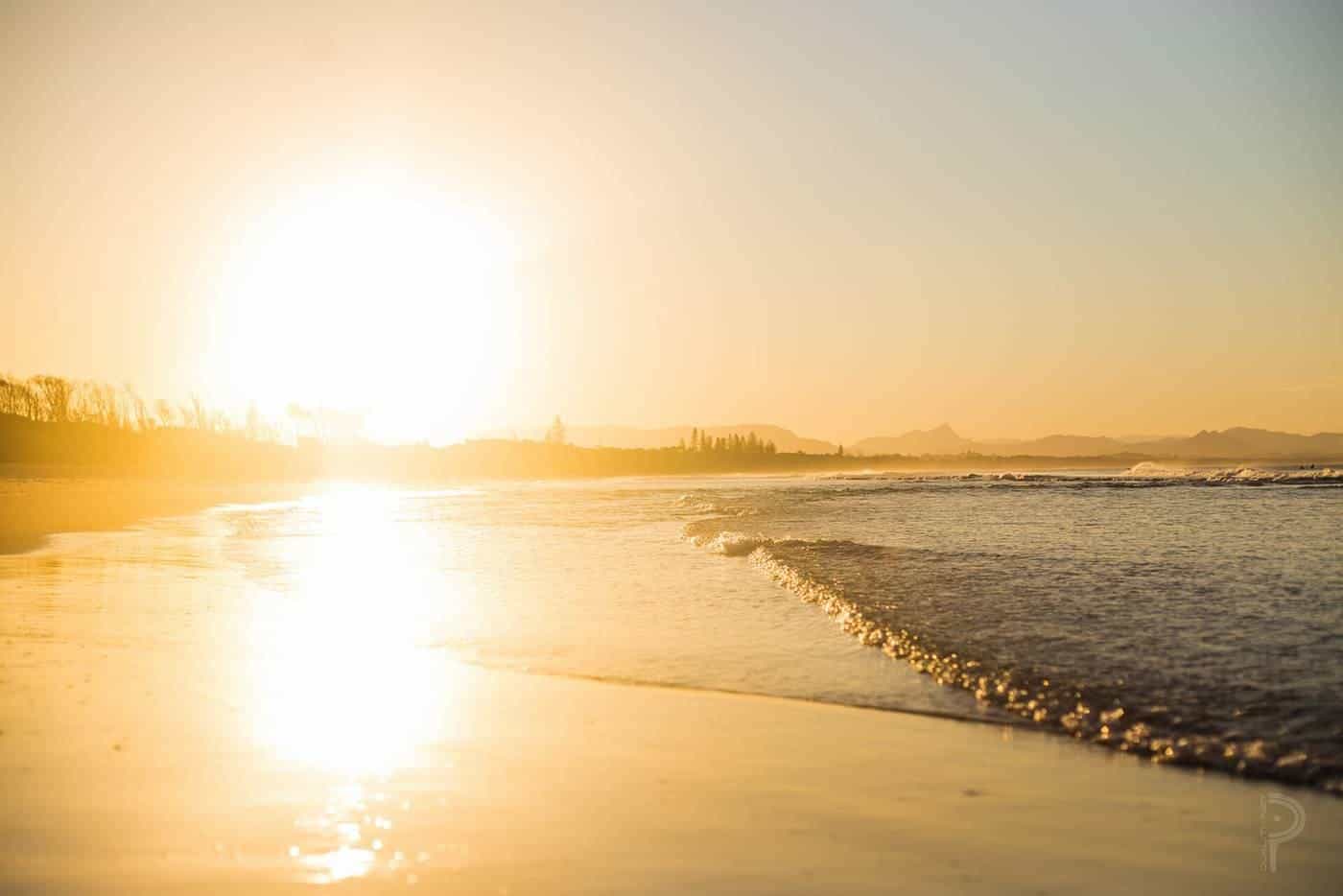 The sun setting over a calm beach and shallow water
