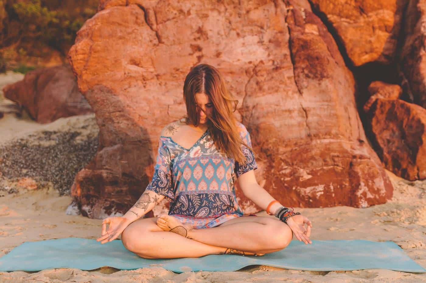 A woman sitting cross-legged on a yoga mat in front of red sandstone rocks