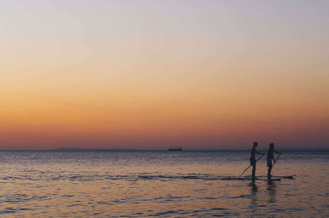 Two people paddleboarding on a calm sea at sunset
