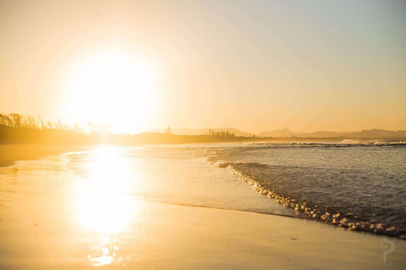 The sun setting over a calm beach and shallow water