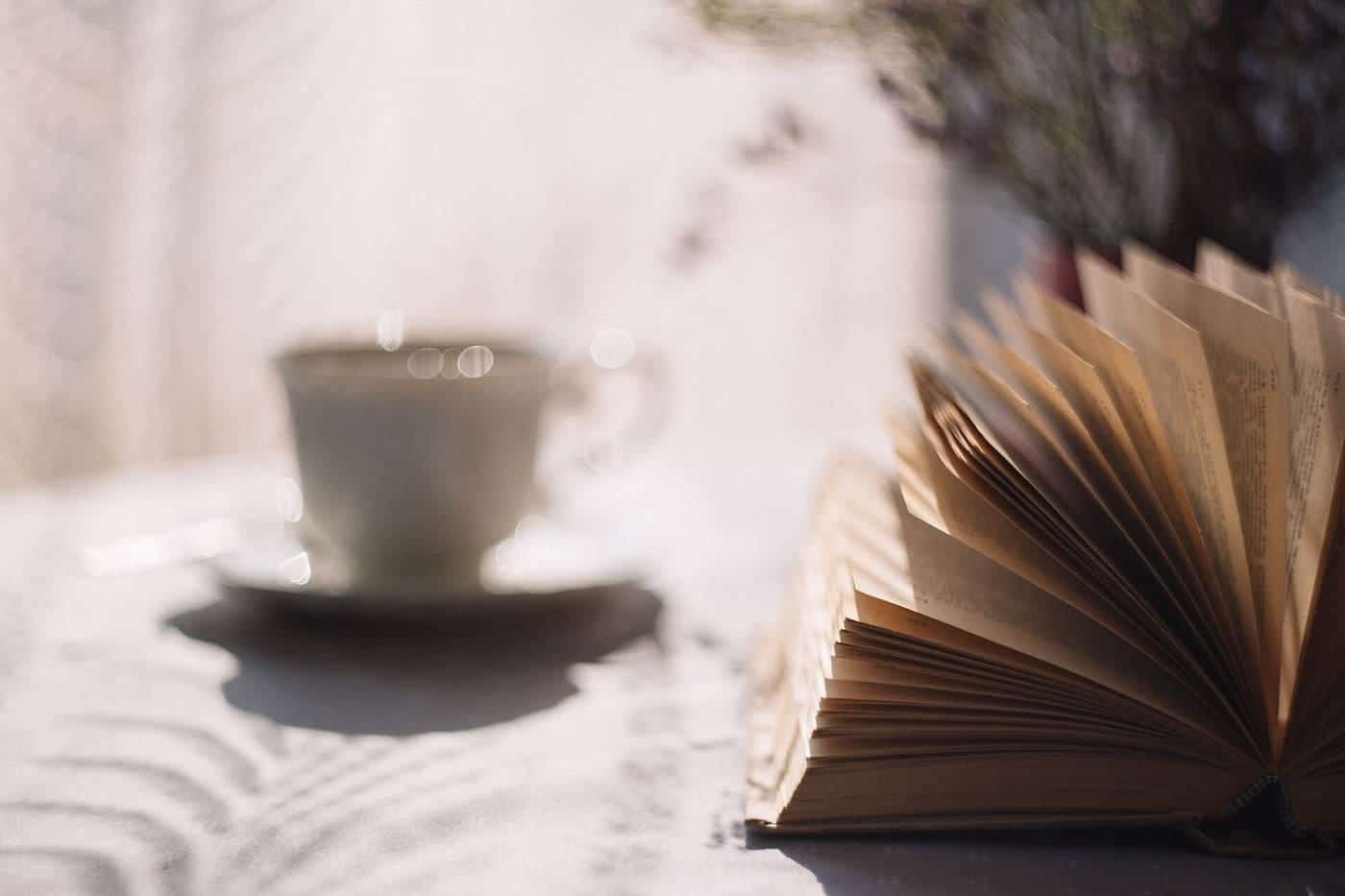 An open book beside a white cup of tea on a table