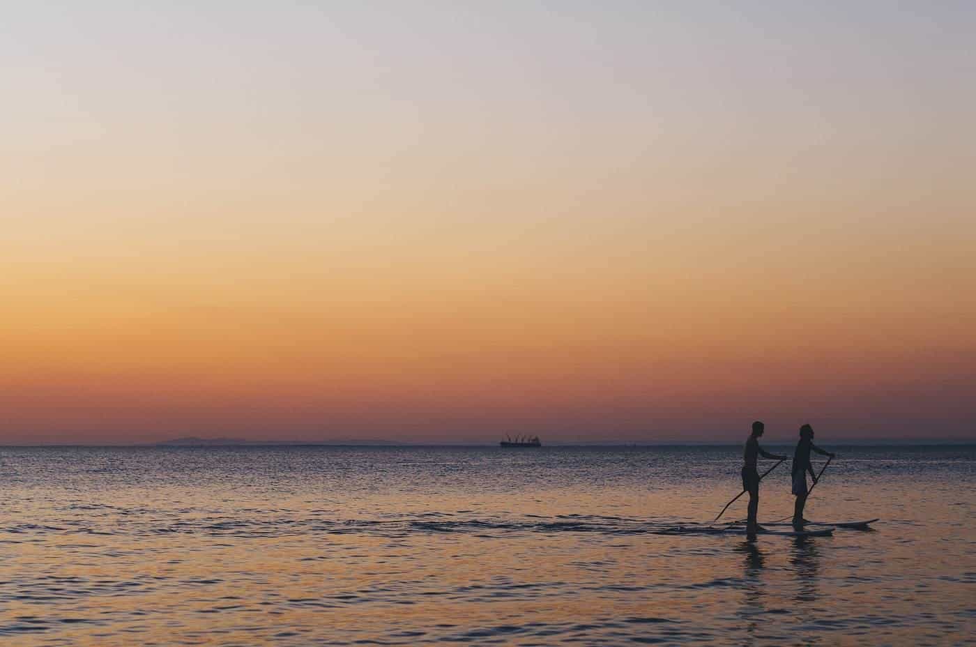 Two people paddleboarding on a calm sea at sunset